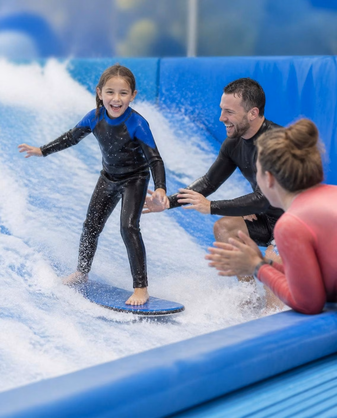 A young child standing up on the wave for the first time, coach beside them